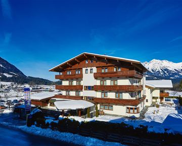Ein charmantes Gebäude im Alpenstil umgeben von Schnee und Bergen. Der Himmel ist klar und blau, was eine einladende Atmosphäre schafft.