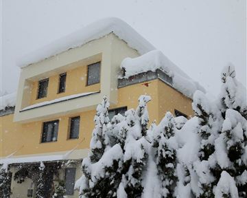 Ein großes Gebäude, das von einer dicken Schicht Schnee bedeckt ist. Im Vordergrund sind schneebedeckte Bäume zu sehen.