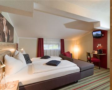 A cozy room with two beds, a sofa, and a desk. Bright colors and a window create a friendly atmosphere.