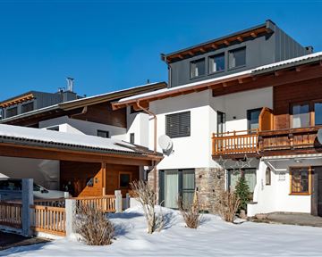 A modern house in the snow with a wooden balcony and clear blue sky. The surroundings feel calm and welcoming.