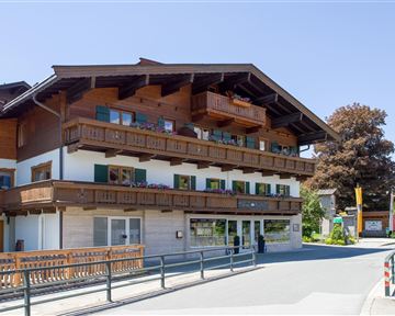 A charming building in alpine style with balconies and a wooden-clad facade. It is located on a quiet street in a picturesque setting.