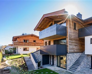 Ein modernes Haus mit Holz- und Steinverkleidung. Im Hintergrund sind weitere traditionelle Gebäude zu sehen.
