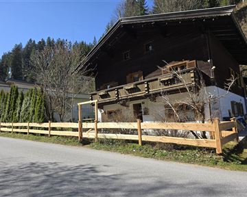 Ein traditionelles Holzhaus mit einem Balkon und einem Gartenzaun. Es befindet sich an einer ruhigen Straße, umgeben von Bäumen und der Natur.