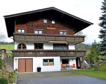 Ein traditionelles zweigeschossiges Haus mit Holzelementen und einem großen Balkon. Der Garten ist gepflegt und es gibt eine Terrasse mit Sitzgelegenheiten.