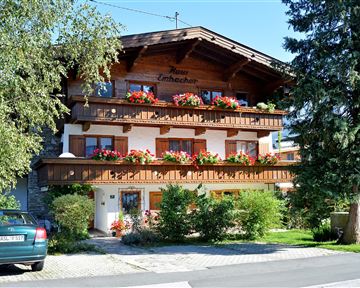A charming building in Alpine style with blooming balcony boxes. Surrounded by green countryside and a clear blue sky.