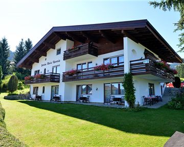 Ein gemütliches Haus mit einem großen Garten und Balkonen. Umgeben von grünen Bäumen und Bergen.