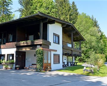 A charming house in a rural setting, surrounded by trees and grass. The clear sky and the sun create a pleasant atmosphere.