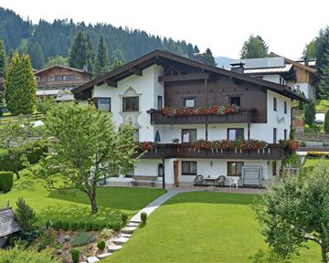 A charming house in alpine style, surrounded by green meadows and trees. The terrace is adorned with blooming flowers.