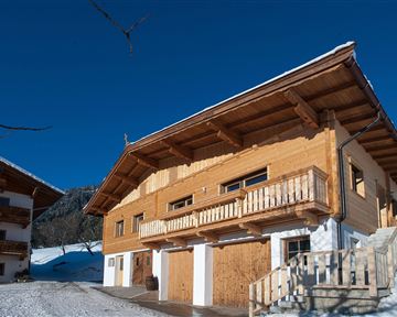 Ein Holzhaus im Schnee mit einem klaren blauen Himmel. Die Architektur ist traditionell und gemütlich.