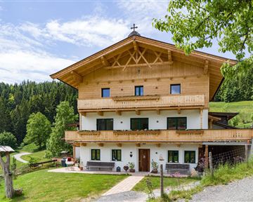 Ein traditionelles Holzhaus in den Bergen, umgeben von grünen Wäldern. Der klare Himmel und die schöne Landschaft schaffen eine idyllische Atmosphäre.
