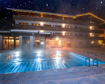 Ein gemütliches Hotelgebäude im Schnee mit einem beleuchteten Pool. Der Nachthimmel ist klar und sternenklar.
