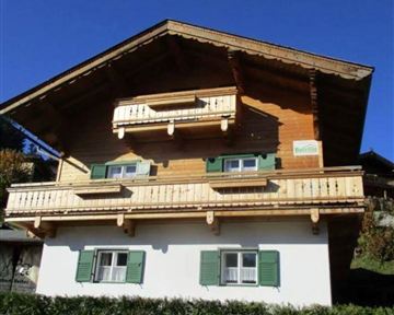 Ein charmantes Holzhaus mit einem Dach aus Ziegeln. Es hat grüne Fensterläden und zwei Balkone.