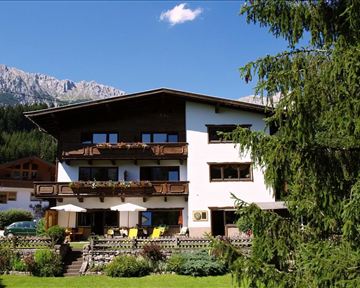 Ein charmantes Haus im alpinen Stil, umgeben von Bergen und Bäumen. Die sonnigen Balkone laden zum Entspannen ein.