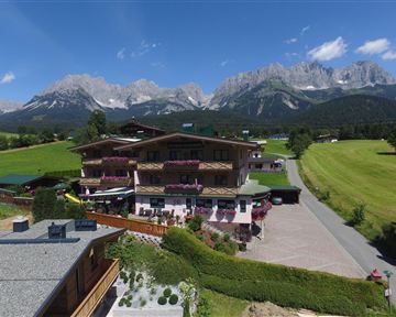 A charming chalet in the Alps with blooming balconies. In the background, majestic mountains rise under a clear blue sky.