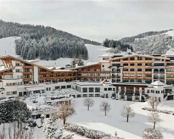 Ein großes, modernes Hotel in einer verschneiten Landschaft. Im Hintergrund sind schneebedeckte Berge und Nadelbäume zu sehen.