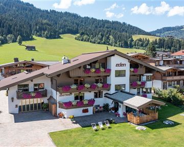 A cozy hotel with blooming balcony boxes amidst a green landscape. In the background, gentle hills and a clear sky are visible.