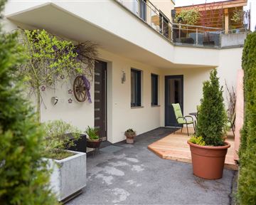 Ein einladender Eingangsbereich mit Pflanzen und einer Holzterrasse. Auf der Terrasse steht ein Stuhl, um die frische Luft zu genießen.