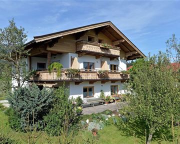 A charming country house with various balconies and many flowers. Surrounded by lush greenery and trees, it is inviting and friendly.