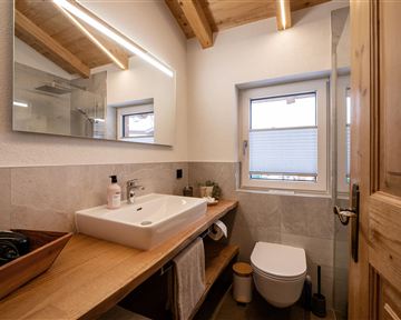 Ein modernes Badezimmer mit Holzdetails und einer eleganten Waschgelegenheit. Helle Wände und ein Fenster sorgen für ausreichend Tageslicht.