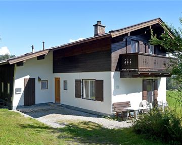 A cozy house with a balcony in a rural setting. The meadow is green and the sky is clear.