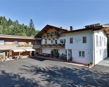 Ein charmantes Gebäude im alpinen Stil mit Balkonen und einer einladenden Fassade. Umgeben von Bäumen und Bergen in klarem blauen Himmel.