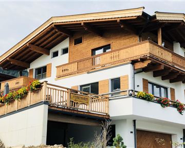 Ein modernes Chalet mit Holzverkleidung und mehreren Balkonen. Bunte Blumen schmücken die Fassade und sorgen für eine einladende Atmosphäre.