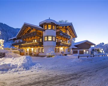 A charming chalet in the snow, surrounded by a wintry landscape. Soft lighting creates a cozy atmosphere at dusk.