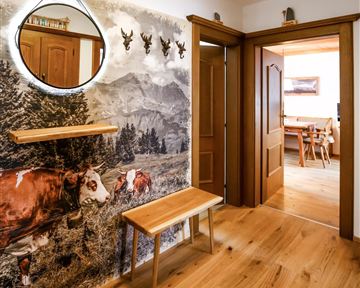 An inviting hallway with a wooden floor and a teardrop-shaped mirror. On the wall, there is a friendly Alpine motif featuring cows and mountains.