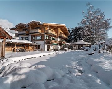A beautiful building in winter with a snow-covered garden. The sky is blue and the landscape looks peaceful.