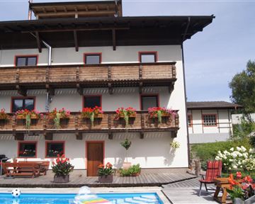 Ein hübsches Haus mit Balkonen und blühenden Pflanzen. Der Swimmingpool im Vordergrund lädt zum Entspannen ein.