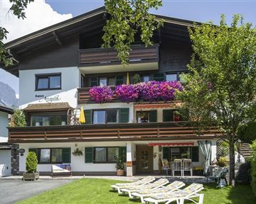 Ein charmantes Gasthaus mit üppigen Blumen und einem gepflegten Garten. Liegen stehen bereit, um die sonnige Umgebung zu genießen.