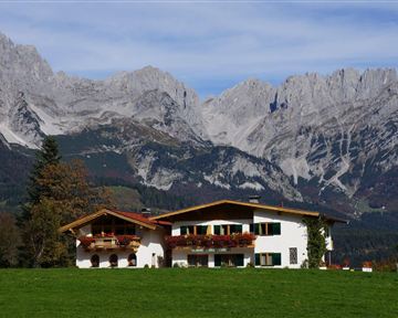 A beautiful house in the Alps, surrounded by green meadows and impressive mountains. The sky is clear and nature radiates tranquility.