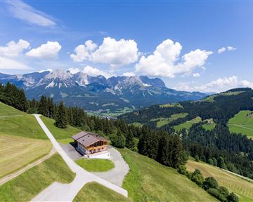 Ein wunderschönes Bergpanorama mit grünen Wiesen und einem einsamen Chalet. Die Wolken am Himmel verleihen der Szenerie ein malerisches Flair.