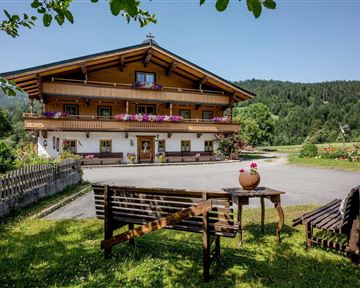 Ein charmantes Alpenhaus mit blühenden Fensterbänken. Im Vordergrund stehen Gartenmöbel auf einer grünen Wiese.