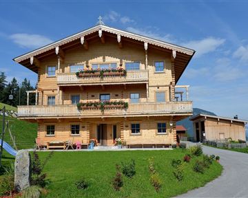 Ein schönes Holzhaus in den Bergen mit einem gepflegten Garten. Der Himmel ist blau und die Umgebung ist grün.