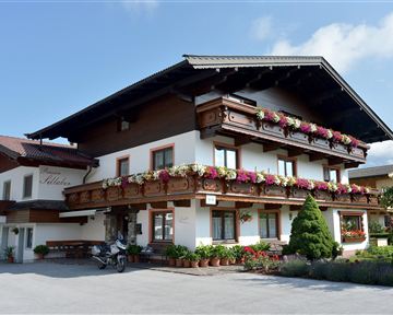 Ein traditionelles alpenländisches Haus mit einem schönen Balkon voller Blumen. Die Fassade ist hell und einladend, umgeben von grünem Garten.