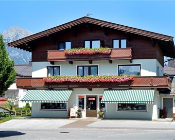 Ein charmantes Gebäude mit Holzverkleidung und bunten Blumen am Balkon. Im Hintergrund ist eine schöne Berglandschaft zu sehen.