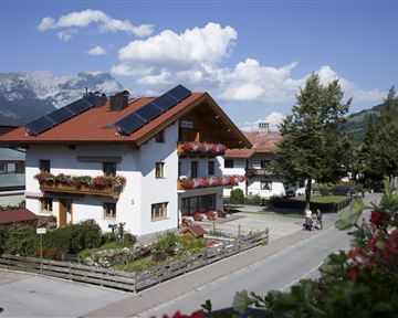 A beautiful house with flower boxes and solar panels. In the background, mountains and a clear sky are visible.