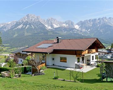 A picturesque landscape with a modern house and mountains in the background. The garden is green and inviting, ideal for a peaceful getaway.