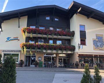 Ein charmantes Gebäude mit bunten Blumenbalkonen. Im Erdgeschoss befinden sich ein Café und eine Konditorei.