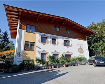 Ein charmantes zweistöckiges Gebäude mit einer bemalten Fassade. Vor dem Haus stehen viele Pflanzen und ein geparkter Wagen.