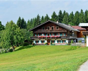 A traditional wooden house in a green landscape.  
Surrounded by trees and meadows under a clear sky.
