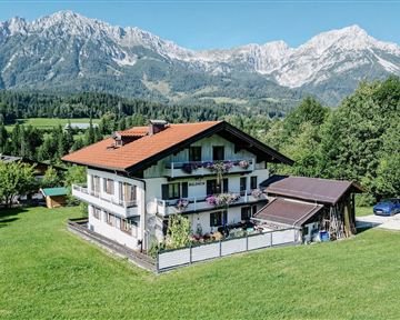 Ein schönes Haus in einer grünen Landschaft mit Blick auf die Berge. Der Himmel ist klar und die Umgebung ist ruhig und einladend.