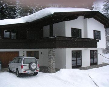 Ein modernes Haus im Schnee mit einem begrünten Dach. Ein Auto steht auf der Einfahrt vor dem Gebäude.