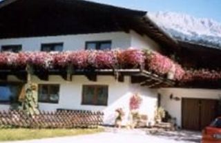 Ein charmantes Haus mit einem Balkon voller Blumen. Im Hintergrund sind die Berge sichtbar und der Himmel ist klar.