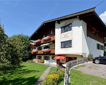 Ein malerisches Haus im alpinen Stil umgeben von Grün. Es bietet Balkone mit Blumen und einen gepflegten Garten.