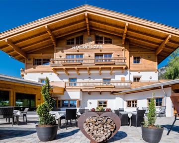 Ein charmantes Holzgebäude im alpinen Stil mit einem großen Vordach. Terrassenmöbel und Pflanzen laden zum Verweilen ein.