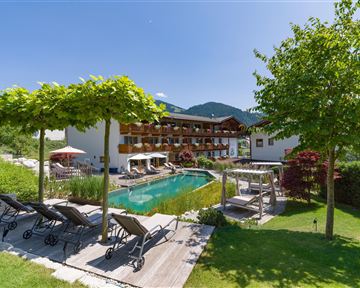 Exterior view of Hotel Alpenpanorama with garden, pool, sun loungers, and view of the Tyrolean mountains.