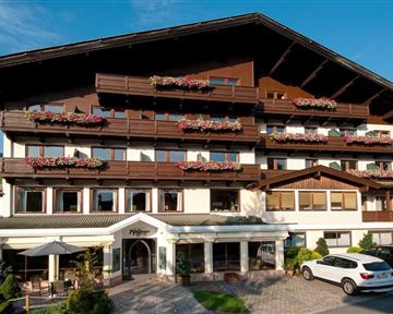 A charming hotel building with balconies and floral decorations. The sunny surroundings and the mountain landscape give the place an inviting atmosphere.