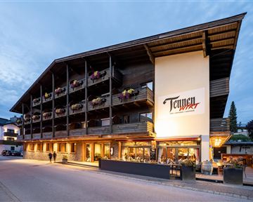 A modern hotel building with a traditional wooden design. There are balconies with flowers and an inviting atmosphere.